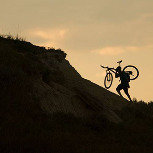 Person carrying bike up a steep badlands formation