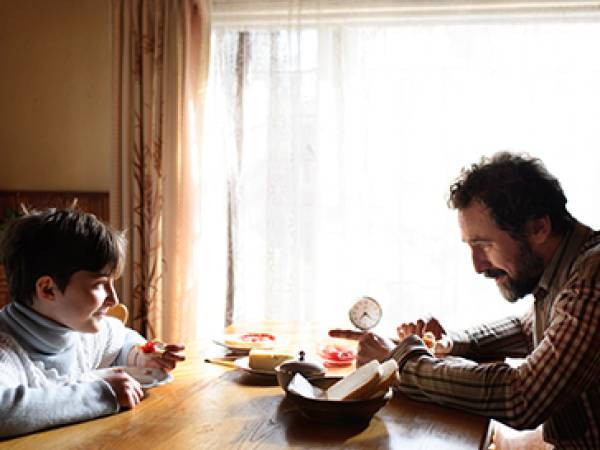 Single father and child sit at a kitchen table