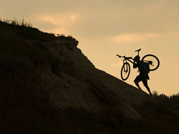 Person carrying bike up a steep badlands formation