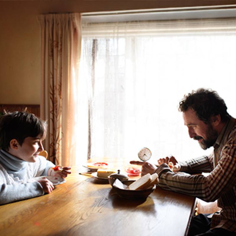 Single father and child sit at a kitchen table