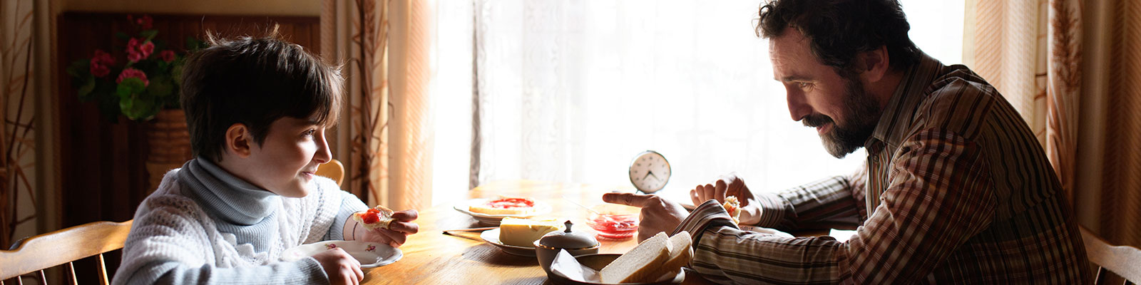 Single father and child sit at a kitchen table eating breakfast