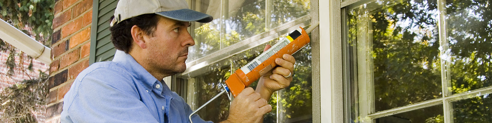 Man repairing a window on the outside of a home