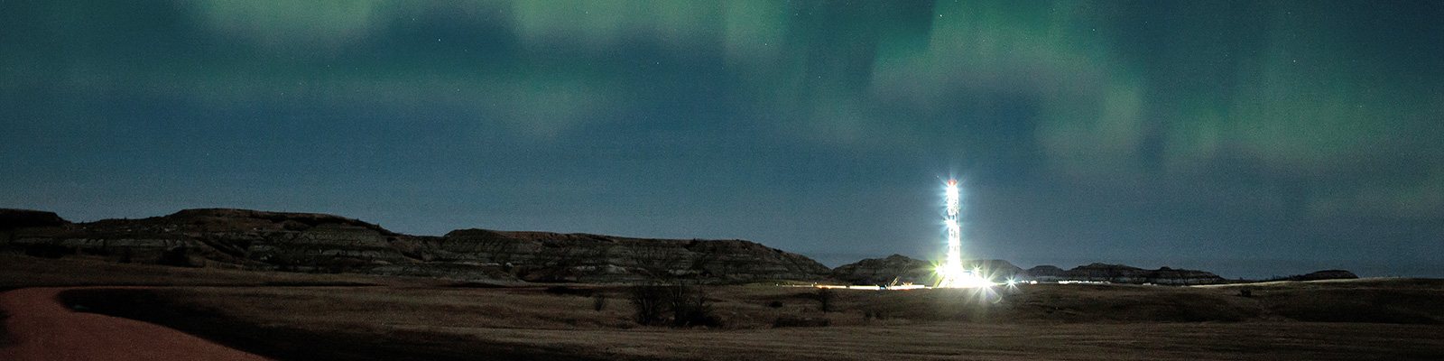 Oil field lit up at night, near Mandaree, with northern lights in the background