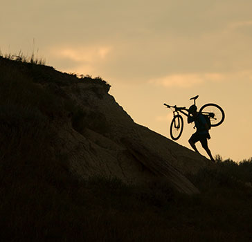 Person carrying bike up a steep badlands formation