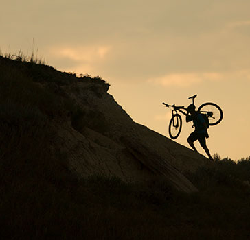 Person carrying bike up a steep badlands formation