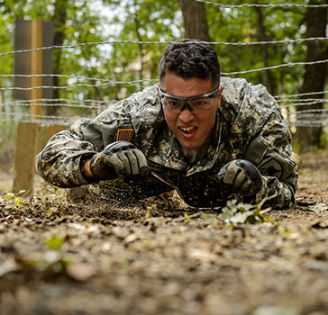 A soldier crawls through a portion of an obstacle course