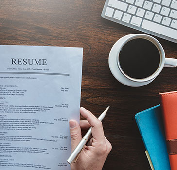 Resume draft on a desk near a cup of coffee, some folders and a keyboard