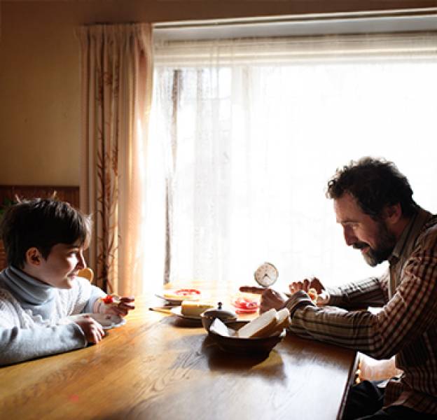 Single father and child sit at a kitchen table